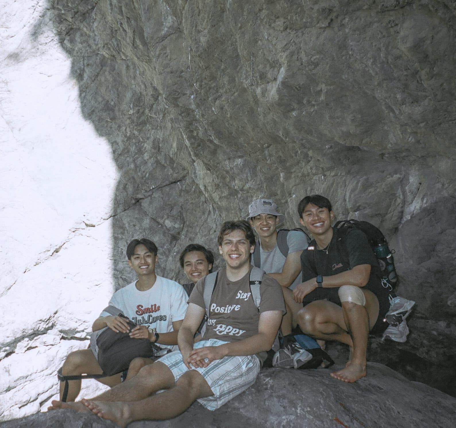 A group of friends sitting under a rock overhang on a hike